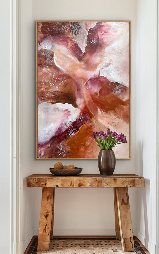 Abstract art piece on a wall above a wooden console table with a vase and fruit.